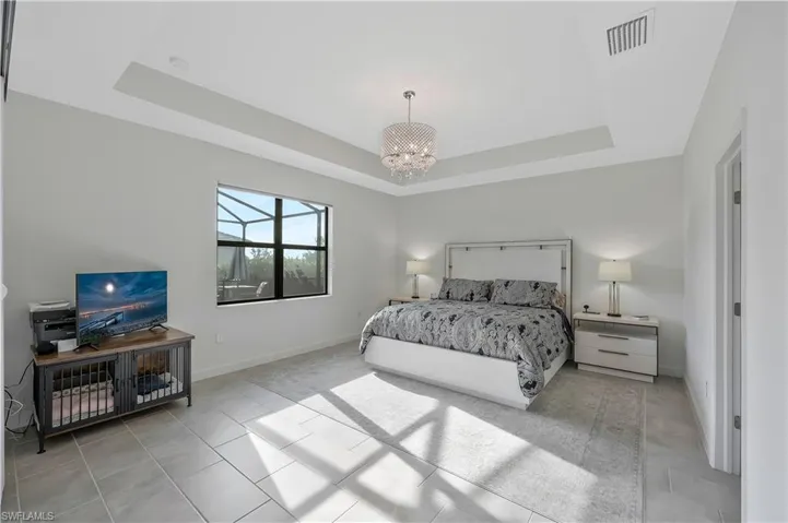 Bedroom with a tray ceiling, baseboards, a chandelier, and visible vents
