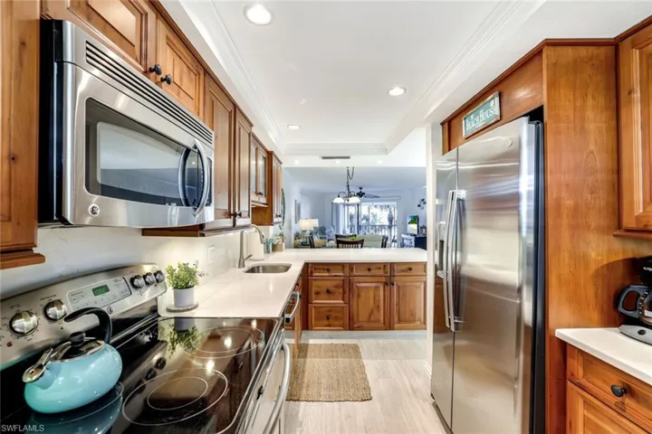 Kitchen featuring wood finish cabinets, stainless steel appliances, ornamental molding, decorative light fixtures, and a peninsula