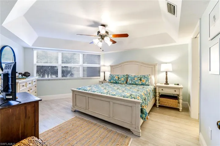 Bedroom with a tray ceiling, light wood-style floors, multiple windows, and ceiling fan