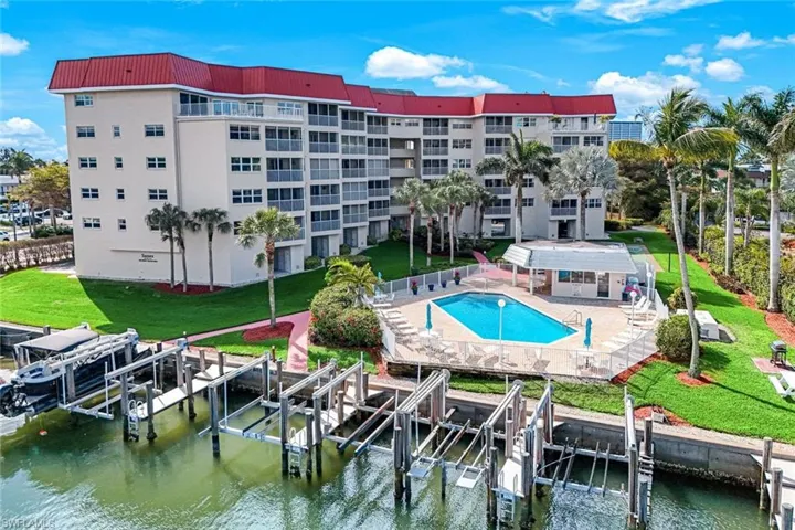 Community pool with boat lift, a water view, a dock, a patio area, and a lawn