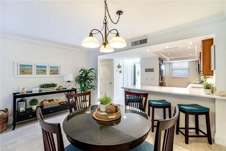 Dining room featuring crown molding, light wood-style flooring, suspended lighting, and a raised ceiling
