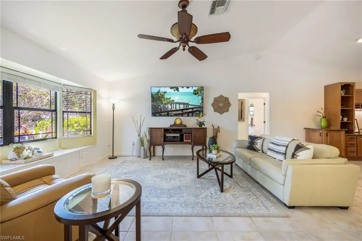 Living room featuring open floor plan, bay window, vaulted ceiling, and light tile patterned floors. Painted in light, neutral pallet throughout.