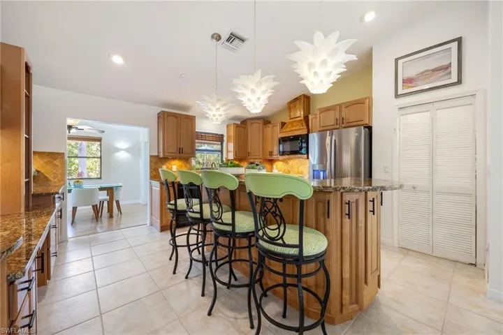 Kitchen with Custom wood cabinets, Granite counters, large kitchen island, Stainless steel appliances. Look at those island lights! Loads of storage and built in work space on left. the bi-fold doors open to walk-in pantry.