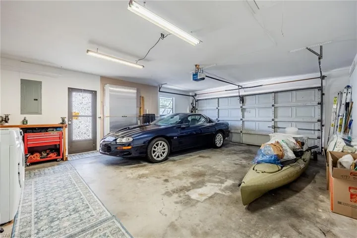 Garage with a garage door opener and electric panel. Oversized garage to accomodate mini workshop, lots of storage. Far wall shows the window/door hurricane shutters and all window screens.