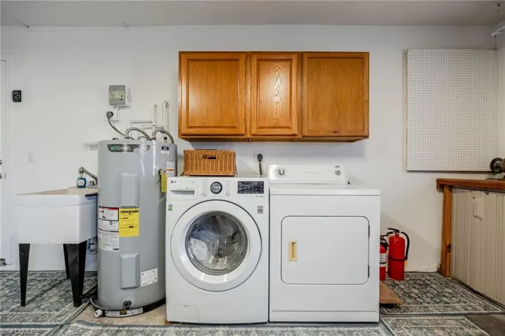 Laundry area featuring cabinet space, electric water heater, and washer and clothes dryer located in the garage.