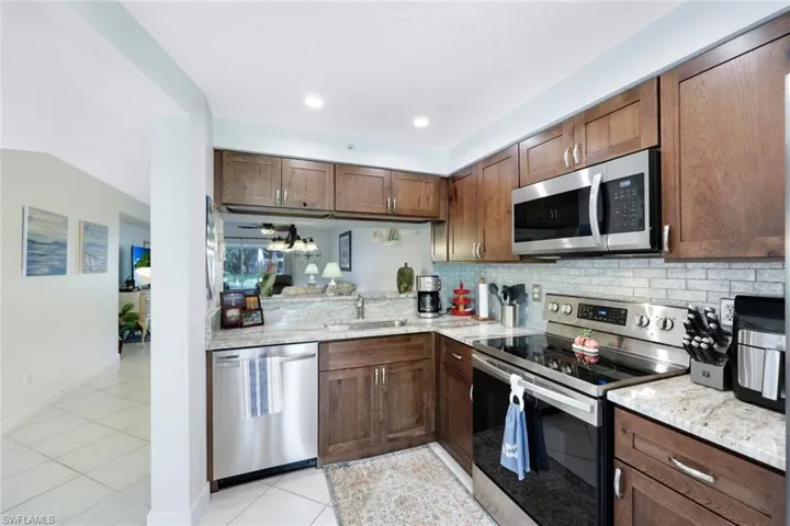 Kitchen with appliances with stainless steel finishes, tasteful backsplash, sink, light stone counters, and light tile patterned flooring