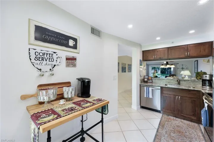 Kitchen with appliances with stainless steel finishes, light tile patterned floors, light stone countertops, and dark brown cabinetry