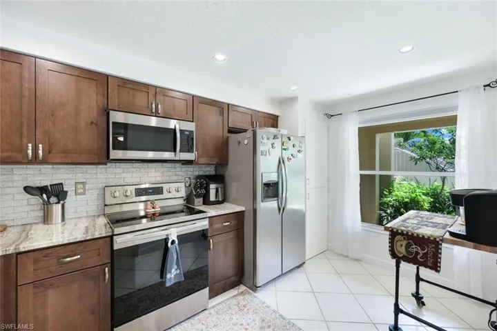 Kitchen featuring appliances with stainless steel finishes, tasteful backsplash, dark brown cabinets, light stone countertops, and light tile patterned flooring
