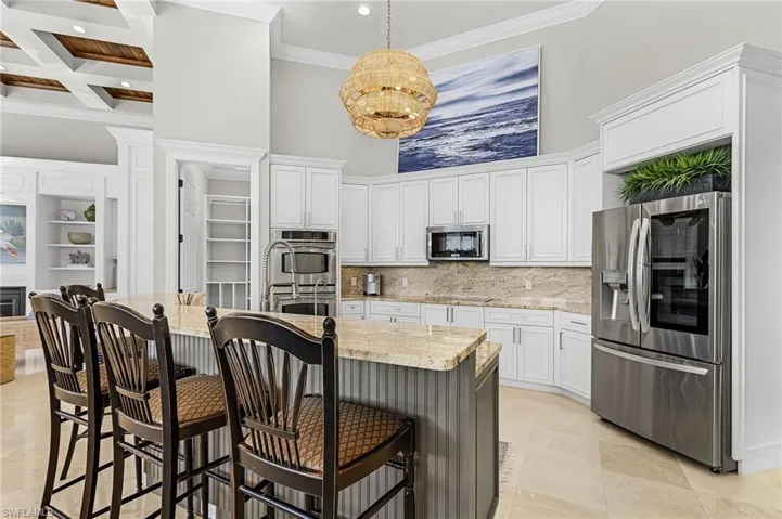 Kitchen with a towering ceiling, granite countertops, marble floors, stainless steel appliances, white cabinetry, and hanging light fixture.