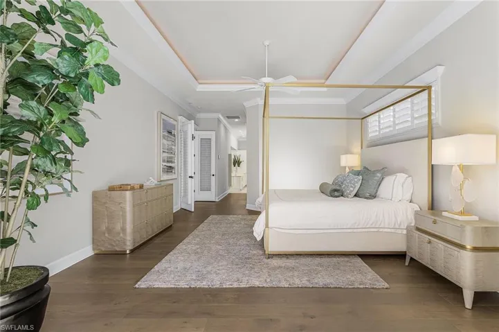 Main bedroom with lighted tray ceiling, crown molding, Vietnamese wood flooring, and  ceiling fan.