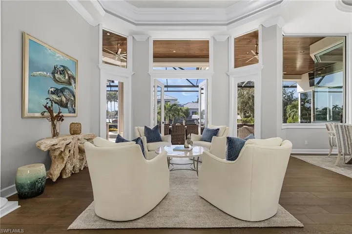 Living room with view of pool and water with coffered ceiling.