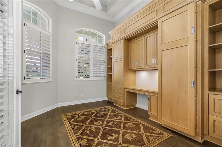 Office with built in study area, built in shelves, dark wood finished floors, and ornamental molding