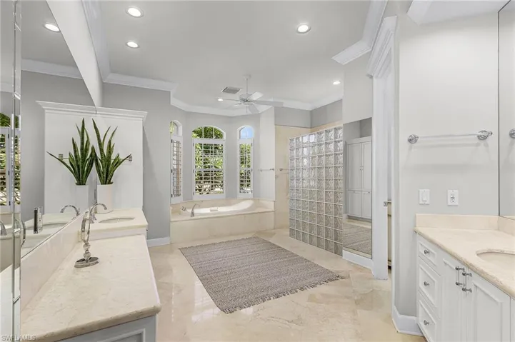 Main bath featuring two sinks, vanity, jetted tub, ornamental molding, recessed lighting, and a walk in shower