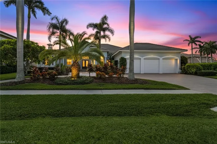 View of front of home at dusk, featuring driveway, manicured lawn, 3 car garage, stucco siding, and tile roof.