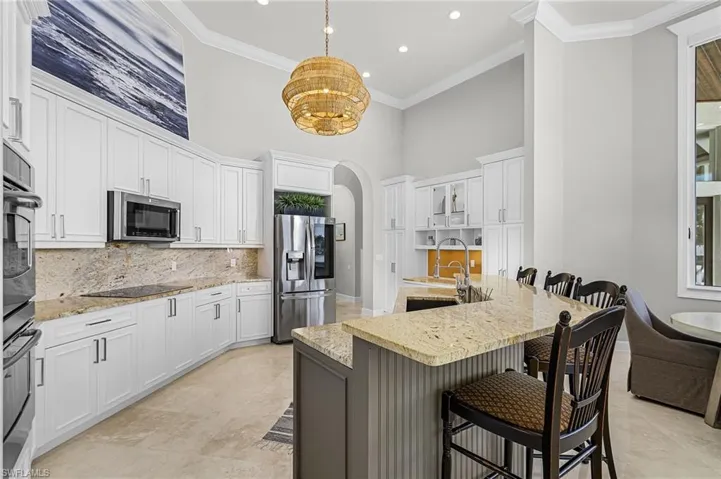 Kitchen with white cabinets, arched walkways, granite countertop breakfast bar, a high ceiling, and ornamental molding