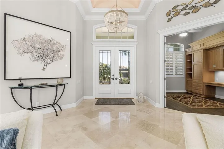 Foyer entrance featuring a towering coffered ceiling, crown molding, a chandelier, french doors, and view of den with built in desk. Marble flooring