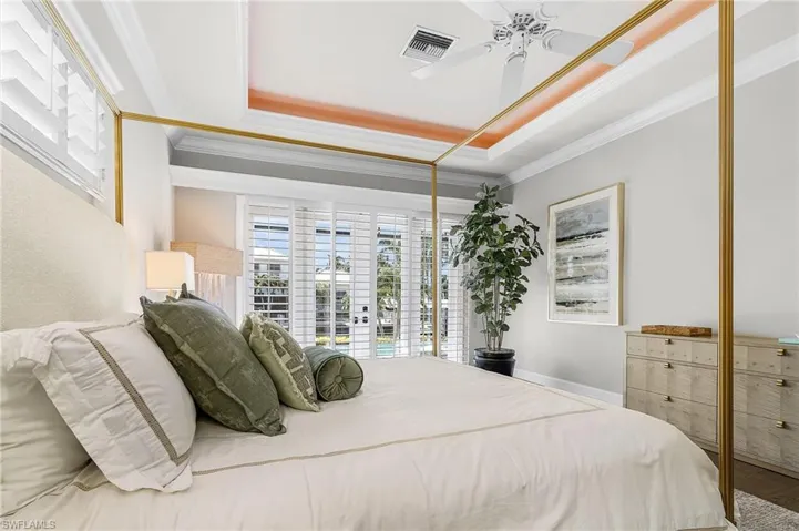 Main bedroom featuring crown molding, a lighted tray ceiling, access to lanai, a ceiling fan, and Vietnamese wood floors