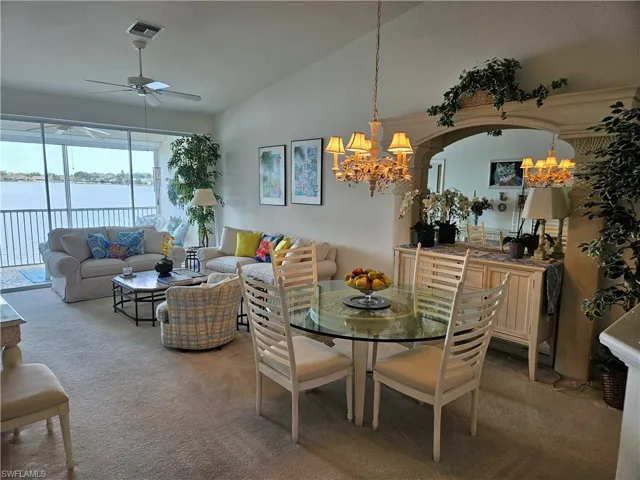Dining room with vaulted ceiling, a water view, carpet floors, and ceiling fan with notable chandelier