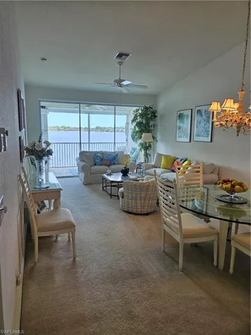 Carpeted dining area with ceiling fan with notable chandelier and a water view