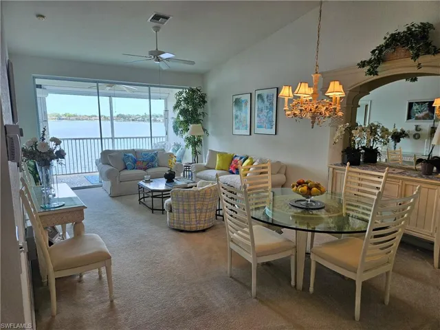 Carpeted dining space with a water view, vaulted ceiling, and ceiling fan with notable chandelier