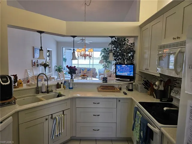 Kitchen featuring white range with electric cooktop, pendant lighting, a chandelier, sink, and light tile floors