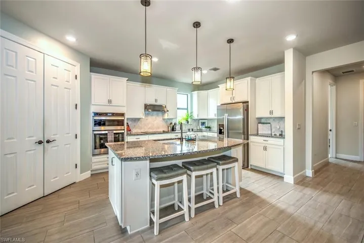 Kitchen with white cabinets, stainless steel appliances, a kitchen island with sink, and dark stone countertops