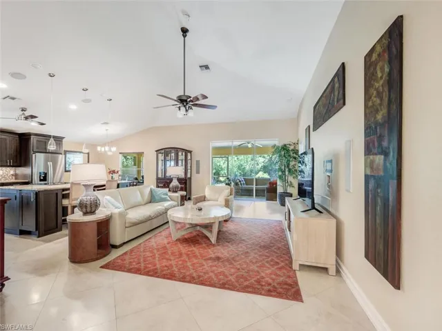 Tiled living room featuring vaulted ceiling and ceiling fan with notable chandelier
