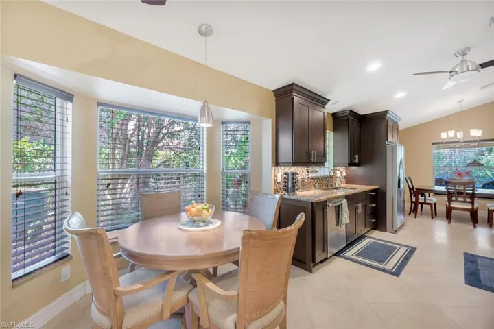 Dining space featuring ceiling fan with notable chandelier, light tile flooring, sink, and lofted ceiling