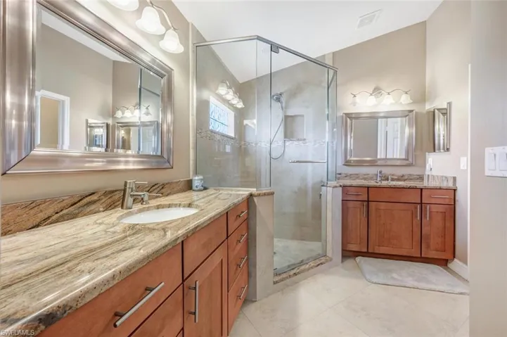 Bathroom with tile floors, a shower with door, vanity with extensive cabinet space, and dual sinks