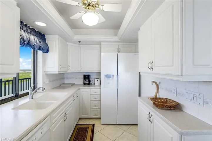 Kitchen featuring white appliances, light tile patterned flooring, ceiling fan, backsplash, and a tray ceiling