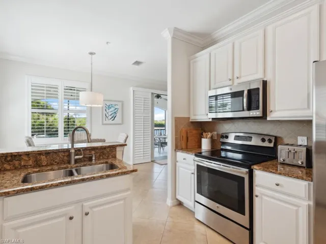 Kitchen with tasteful backsplash, crown molding, light tile patterned flooring, appliances with stainless steel finishes, and a sink