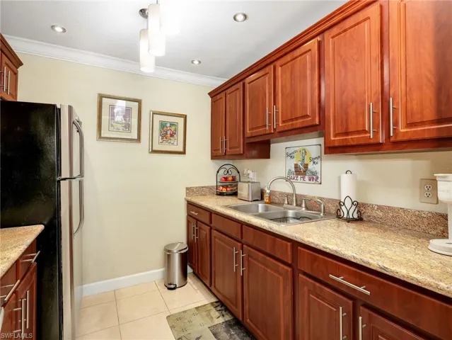 Kitchen with freestanding refrigerator, light stone countertops, ornamental molding, light tile patterned flooring, and hanging light fixtures
