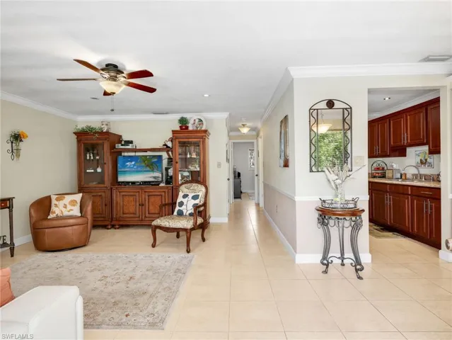 Living room featuring light tile patterned floors, ceiling fan, and ornamental molding