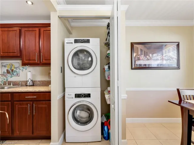 Laundry area featuring light tile patterned floors, stacked washer and dryer, and ornamental molding