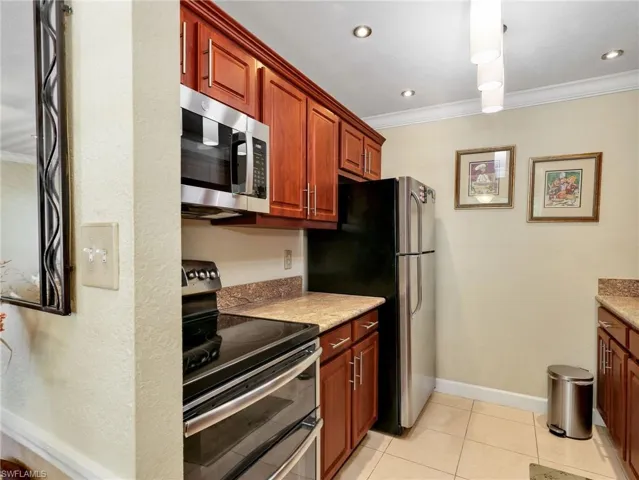Kitchen featuring stainless steel appliances, ornamental molding, light tile patterned floors, light stone counters, and wood finish cabinetry