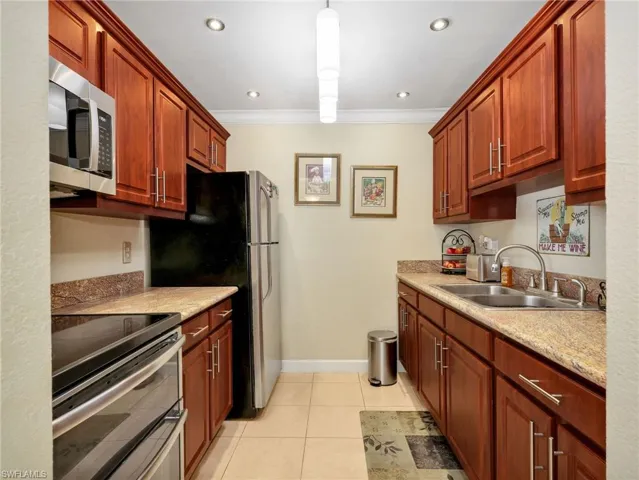 Kitchen featuring stainless steel appliances, crown molding, light tile patterned flooring, light stone countertops, and hanging light fixtures