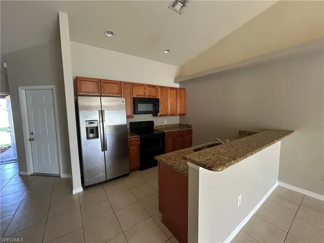Kitchen featuring brown cabinetry, black appliances, light tile patterned floors, vaulted ceiling, and a peninsula