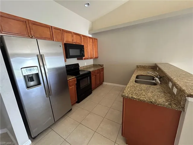 Kitchen featuring black appliances, dark stone countertops, a peninsula, lofted ceiling, and light tile patterned floors