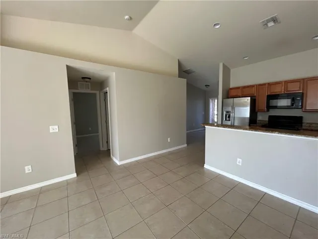 Kitchen featuring brown cabinets, vaulted ceiling, black appliances, light tile patterned floors, and dark stone counters