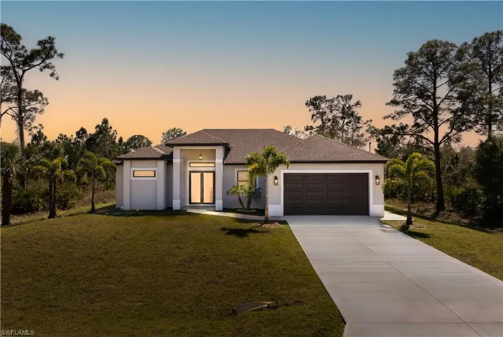 View of front facade featuring concrete driveway, a lawn, an attached garage, and stucco siding