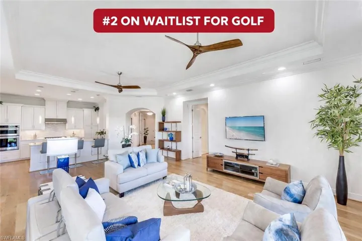 Living room with a tray ceiling, crown molding, arched walkways, recessed lighting, and light wood finished floors