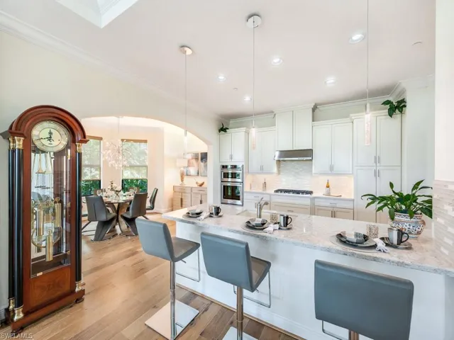 Kitchen featuring hanging light fixtures, a breakfast bar area, a peninsula, light stone counters, and crown molding