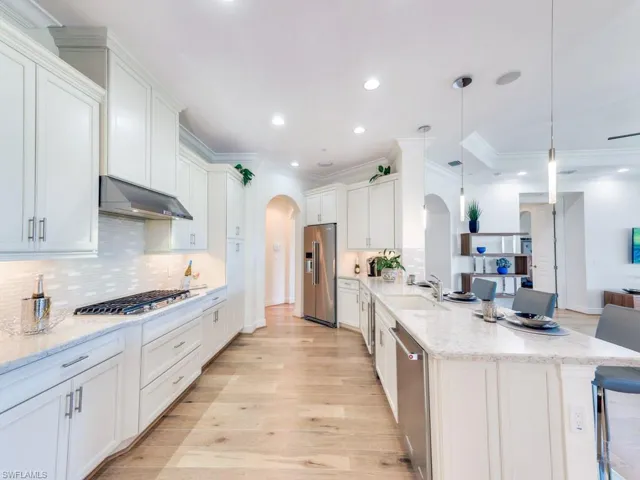 Kitchen with arched walkways, crown molding, light stone countertops, decorative backsplash, and light wood-type flooring