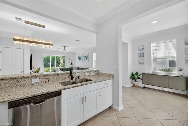 Kitchen with dishwasher, light stone countertops, decorative light fixtures, ornamental molding, and white cabinets