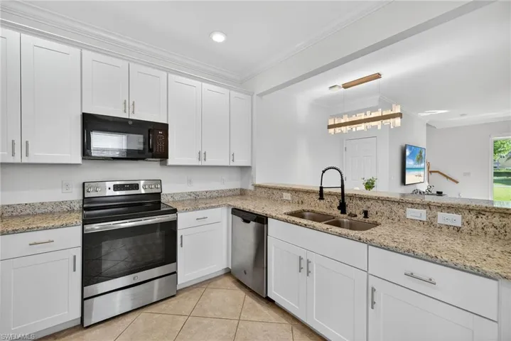 Kitchen with stainless steel appliances, white cabinetry, light stone counters, and ornamental molding