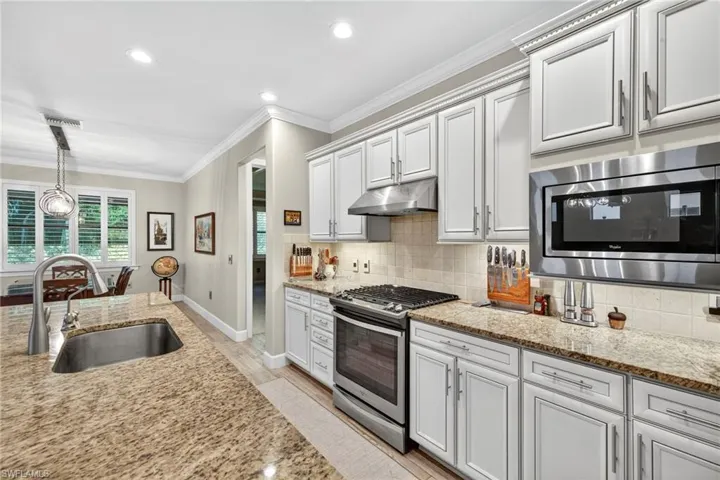 Kitchen featuring tasteful backsplash, stainless steel appliances, crown molding, light stone counters, and pendant lighting