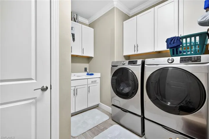 Laundry room with crown molding, washing machine and dryer, light wood finished floors, and cabinet space