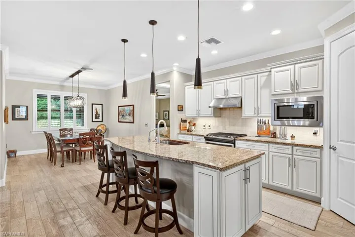 Kitchen with tasteful backsplash, crown molding, light stone countertops, a kitchen island with sink, and pendant lighting