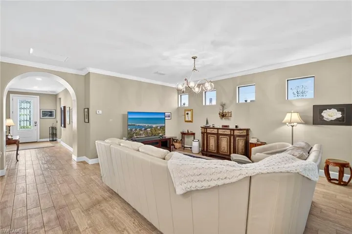 Living room featuring light wood-style flooring, arched walkways, plenty of natural light, ornamental molding, and a chandelier