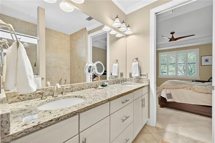 Ensuite bathroom with crown molding, double vanity, light tile patterned flooring, ceiling fan, and light colored carpet